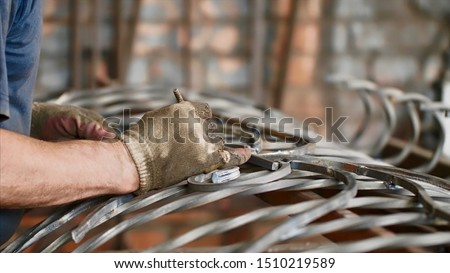 Locksmith at work in fitting shop, hands in gloves closeup. Master makes notes with a pencil on a metal bar measuring it applying to the finished metal fence. Art forging of metal products.
