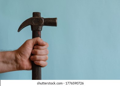 Locksmith's hand holds a vintage hammer with a claw hammer. Male hand with a hammer with a long wooden hilt. Middle-aged man of European race. Hand tool