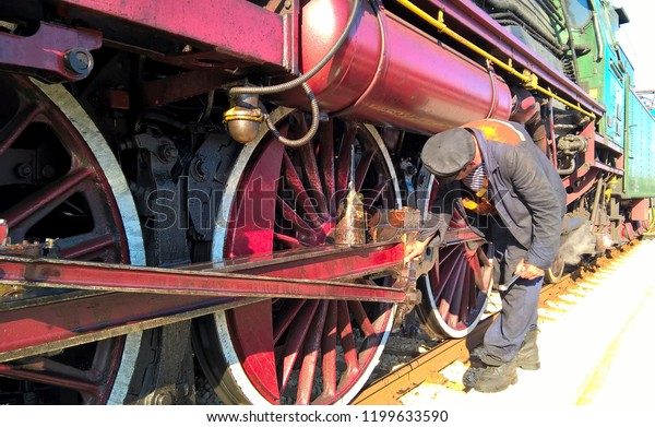 Locomotive driver maintaining steam engine.\
Train mechanic lubricating steam\
machine.