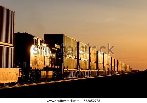 Locomotive and Train Carrying Shipping Containers\
in Golden Sunset on the\
Prairie