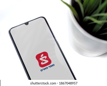 Lod, Israel - July 8, 2020: Modern minimalist office workspace with mobile smartphone with Super Pharm app launch screen with logo in hebrew text on white background. Top view flat lay with copy space