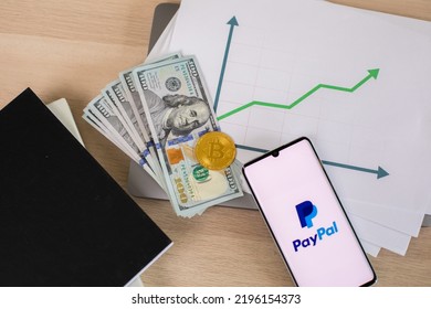 Lodz, Poland - June 21, 2022: Paypal Application On Smartphone Near Dollar Bills And Crypto Currency And And Growing Graph