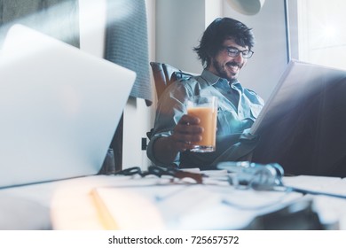 Loft coworking place situation. Young man working with documents in studio, developing new project. Happy and drinking juice. Paperwork and laptop using - Shutterstock ID 725657572