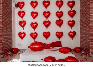 Loft interior in festive style for Valentines Day. Brick walls white bed on floor among red heart shaped balloons with Inscription Love, pillows. Foil balloons with garland. Decorating home for date