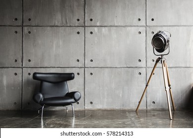 Loft interior mock up photo. Grey block wall with leather black chair and vintage light source lamp. Background photo with copy space for text. 