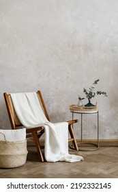Loft interior with white cushion in wicked basket close to wooden chair and home decor on side table. Vertical shot of elegant living room with new furniture in bohemian style against copy space wall