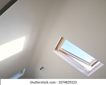 Loft Room Ceiling With Skylight Window With Shadow On Other Side Of Ceiling. Pale Blue Sky Outside Of Window