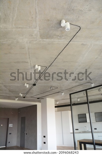 Loft style apartment design with a\
close-up of concrete ceiling, exposed black cables, wires with\
white light lamps, gray wall finishing and glass room divider.\
