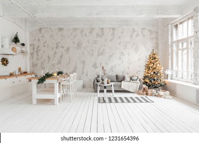 Loft Style Apartment, Large Spacious Living Room With Dining Table And Kitchen. Room With Christmas Tree. Comfortable Sofa, High Large Windows. Light White Brick Wall.