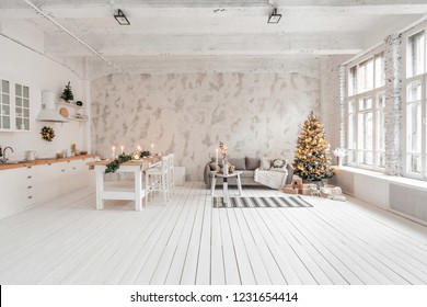 Loft Style Apartment, Large Spacious Living Room With Dining Table And Kitchen. Room With Christmas Tree. Comfortable Sofa, High Large Windows. Light White Brick Wall.