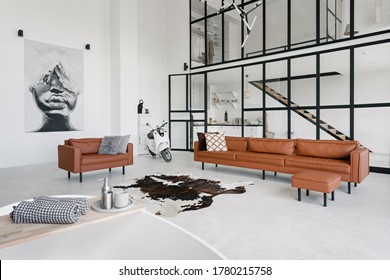Loft style interior in house with modern living room, bath in bathroom, comfortable couch, pillows on leather armchair, painting on wall and scooter on concrete floor with skin carpet - Shutterstock ID 1780215758