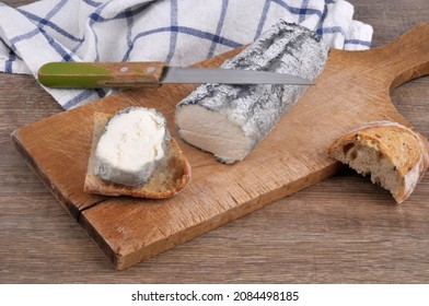 Log Of Ashy Goat Cheese On A Cutting Board With A Knife And Bread