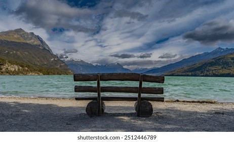 A log bench on the pebbly shore of a beautiful emerald lake. Ripples on the water. Picturesque snow-capped Andes mountains against the blue sky and clouds. Lago Roca. Tierra del Fuego National Park.  - Powered by Shutterstock