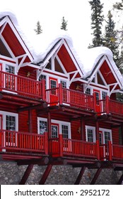 Log Building Of A Mountain Lodge In Winter At Ski Resort With Snowy Roof