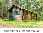 A log cabin with a green door sits in a grassy field. The cabin is surrounded by trees and he is a peaceful retreat