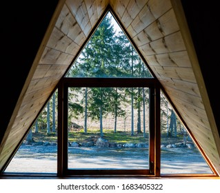 Log cabin window. Looking through the window from inside. Nature behind window glass. Window frame and curtain. Triangle. Timber construction. Wooden, log hut. Warm wooden shack. Sunny weather - Powered by Shutterstock