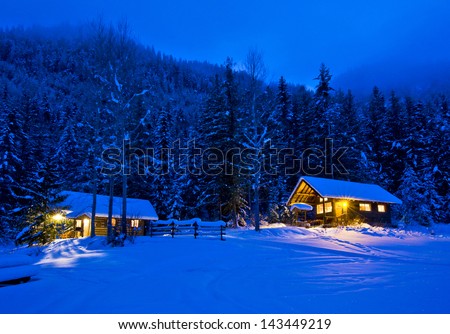 Log cabins glowing in the dusk surrounded by snow.