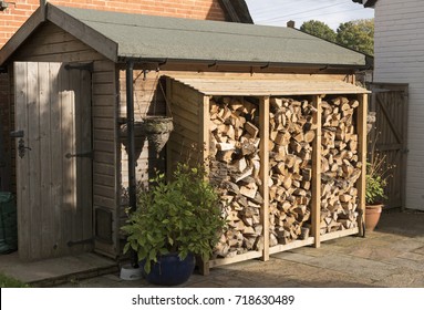 Log Store Standing Against A Garden Shed. Logs Stacked In A Garden. UK