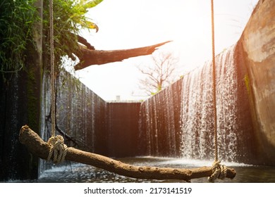 Log Wood Swing With Rope And Place Is The Flowing Water Like A Small Waterfall Curtain. Water Overflowing The Mortar Weir During The Rainy Seasonand Sunlight At Pang Sawan Weir, Uthai Thani, Thailand.