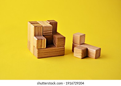 Logical game wooden cube puzzle the last element lies next to the yellow background close up. Solving logical problems. High quality photo