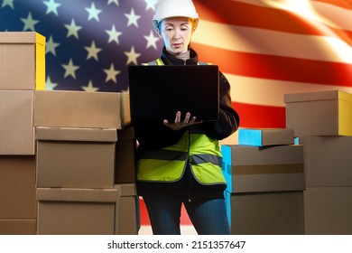 Logistics Business In USA. Woman Logistician In Front American Flag. Woman With Laptop In Protective Helmet. Career In Logistics Business. Employee Of US Courier Company. Delivery Service In America