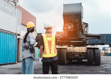 Logistics engineers supervising reach stacker at cargo container yard. Male worker using walkie-talkie and female operator observing operation.