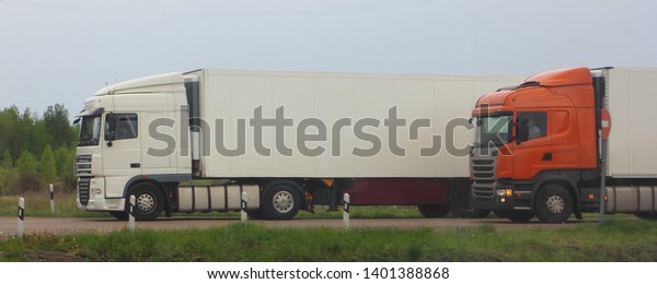 Logistics, international freight by road - two\
european semi trucks drive next to asphalted country road in summer\
day, side view express\
delivery