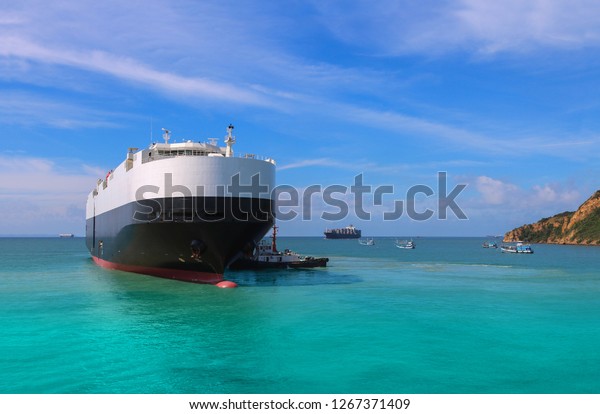 Logistics and international shipping car\
vessels, ocean freight transportation by tugboat assisting the\
vessel to the port on blue sky\
background.