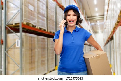 Logistics, Mail Service And Shipment Concept - Happy Smiling Delivery Girl With Parcel Box In Blue Uniform Calling On Smartphone Over Warehouse Background