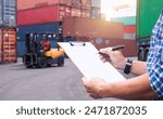 Logistics manager reviewing documents at a shipping yard, with a forklift and cargo containers in the background.