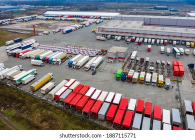 Logistics park with loading hub. Semi-trailer trucks stand on the parking lot and wait for load and unload goods at warehouse ramps. Aerial view at sunset