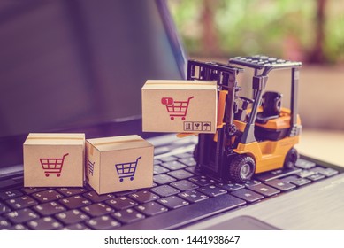 Logistics and supply chain management for online shopping concept : Fork-lift moves a box with a red shopping cart logo, 2 cartons on a laptop computer, depicts delivering goods or products in a store