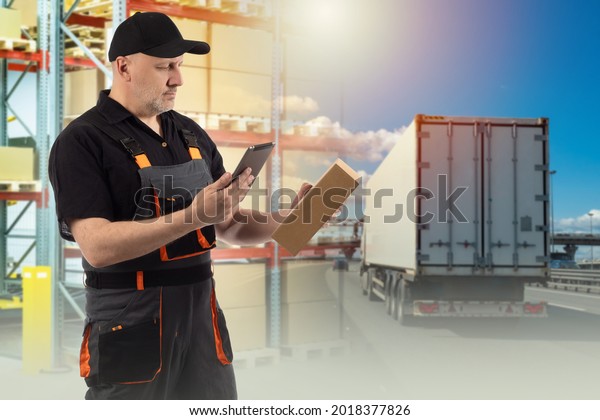 Logistics transport. Worker logistics warehouse.
Worker in a gray uniform. Truck symbolizes logistics transport.
Warehouse worker chooses transport to be shipped. logistician with
phone and box.