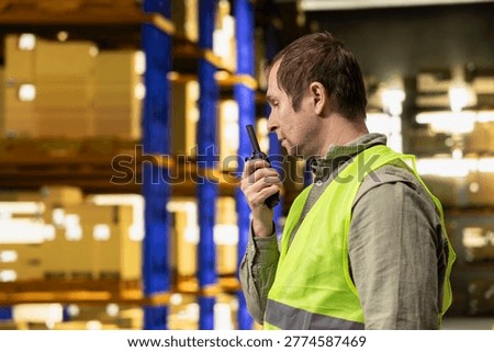 Logistics worker speaking into two-way wireless transceiver near pallets and cardboard boxes. Communication equipment supports order fulfillment workflow and efficient e-commerce operations.