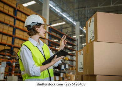 Logistics worker storing package boxes in a large distribution centre,Warehouse worker moving cardboard boxes while working with a colleague in a warehouse,. - Powered by Shutterstock