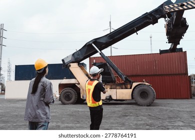 Logistics workers directing reach stacker lifting cargo container. Engineer and operator supervising supply chain transport operation at yard.