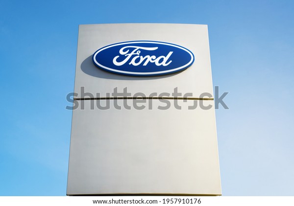 Logo of\
the American automobile construction company Ford outside, against\
a clear blue sky during the day. Signboard of car dealership\
center. Smolensk, Russia\
04.18.2021