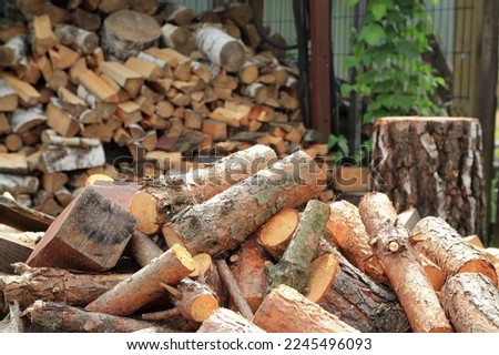 Logs of wood on a pile with chopped wood in the background. 