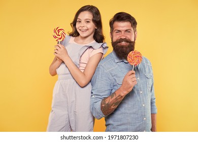 Lollipop a day helps you rest and play. Happy family hold lollipop treats yellow background. Father and child eat lollipop candies. Enjoying large swirl lollipop on sticks. Sweet tooth Candy shop