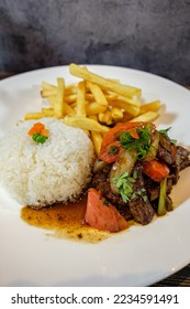 lomo saltado with white rice and french fries, served on wooden table