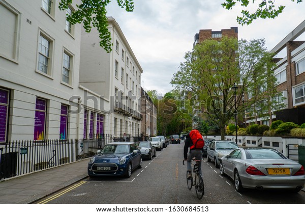 London - 2019: streets of London, cars are\
parked, a man rides a\
bicycle.
