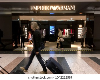 London - 22 August 2017: Woman Pulling A  Wheelie Bag Suitcase In Front Of Luxury High End Retail Store Emporio Armani The London Heathrow Airport (LHR) In London, England.