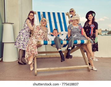 London, England, 05/05/2017, A Group Of Stylish Retro Vintage Fashionable People Sat On A Giant Retro Seaside Deckchair. Giant Deckchair. Best Dressed Award. 