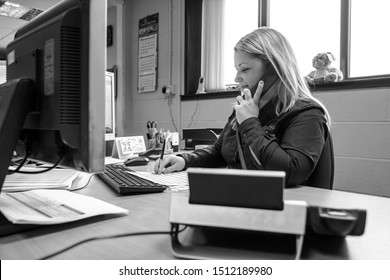 London, England, 28/01/2019 Black and White image of young woman call girl in an administrative role admin work for corporate company in modern office typing on the computer and answering phone calls