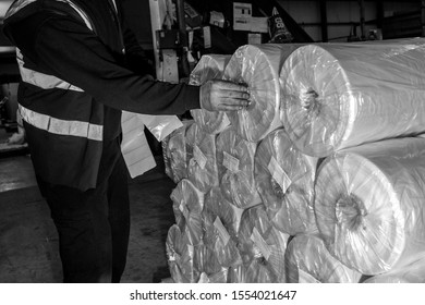 London, England, 28/01/2019 Black & White Image Of A Factory Worker Labelling Up Pallets Stacked With Plastic Wrap In Tubes With Stickers To Mark The Product And Where It Is Being Sent Or Shipped To