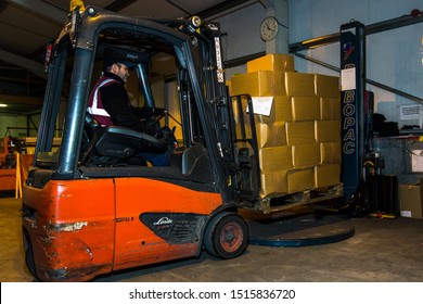 London, England, 28/01/2019 Colour Image Of A Forklift Lifting Wooden Pallet Onto A Rotating Industrial Lazy Susan For Wrapping A Stack Of Boxes Together In Plastic Wrap. Keeping Product Safe 