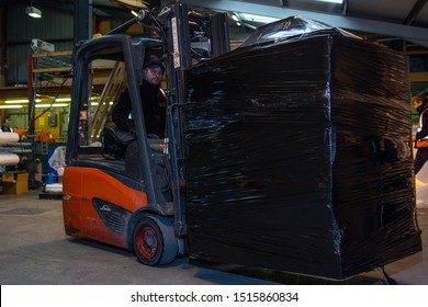 London, England, 28/01/2019 Colour Image Of A Forklift Lifting Wooden Pallet Onto A Rotating Industrial Lazy Susan For Wrapping A Stack Of Boxes Together In Plastic Wrap. Keeping Product Safe 