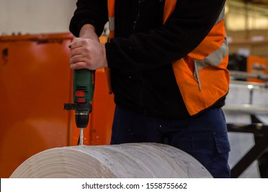 London, England, 28/01/2019 Man In Factory Industrial Condition Drilling Into A Huge Roll Of Plastic Wrap Sheeting With Bosch Drill Wearing Orange High Viability Hi Vis Coat For Safety In Workplace