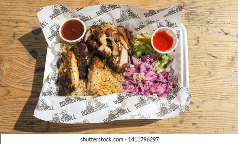 London, England - April 25 2019 - A Street Food Meal Of Jerk Chicken, Coleslaw, Salad And Hot Sauce, On A Wooden Table In Natural Sun Light.  Image Has Copy Space.