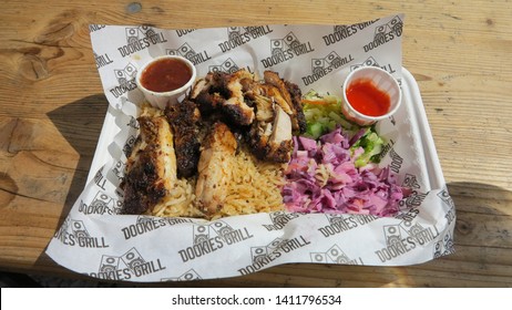 London, England - April 25 2019 - A Street Food Meal Of Jerk Chicken, Coleslaw, Salad And Hot Sauce, On A Wooden Table In Natural Sun Light.  Image Has Copy Space.